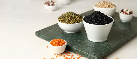 Bowls with different legumes on light background with space for text