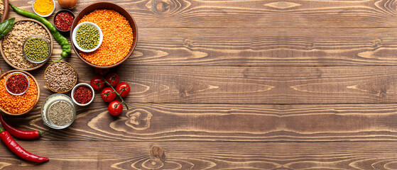 Fototapeta na wymiar Different raw legumes with spices on wooden background with space for text
