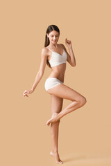 Fototapeta na wymiar Young tanned woman in underwear on beige background