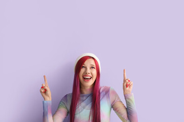Beautiful young woman with bright hair pointing at something on lilac background