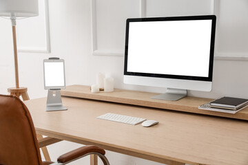 Modern workplace with computer and tablet near light wall