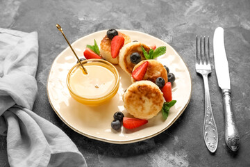 Plate with cottage cheese pancakes, berries and bowl with honey on dark background