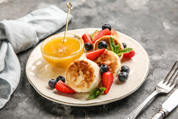 Plate with cottage cheese pancakes, berries and bowl with honey on dark background