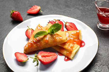 Plate of thin pancakes with strawberries, jam and mint leaves on dark background, closeup