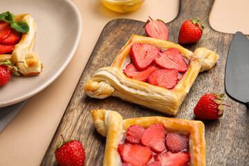 Wooden board with strawberry puff pastry on beige table, closeup
