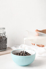 Woman pouring milk from bottle into bowl with tasty cereal rings on light background