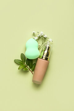 Composition with bottle of makeup foundation and sponge on green background