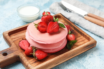 Wooden board with pink pancakes and strawberry on color background, closeup
