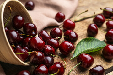 Overturned bowl with ripe cherry on wooden table, closeup