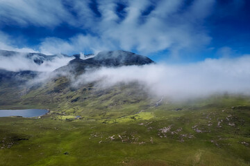 Nature scene in Connemara. Lake and green fields by a tall mountain covered with beautiful cloudy sky. Aerial view. Ireland, Irish landscape and country side.