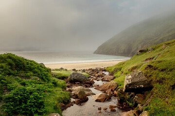 Small water creek flows into ocean. Keem bay and beach in the background in low clouds and fog. Popular travel area with amazing nature scenery. Calm and moody atmosphere.