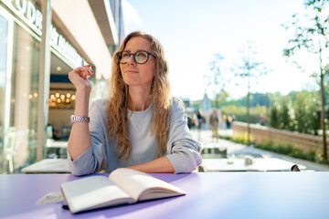 Casual woman sitting at table and taking notes in notebook .on the cafe terrace