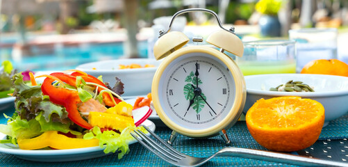 Yellow  alarm clock Intermittent fasting eight hour feeding window concept and eating a healthy food background