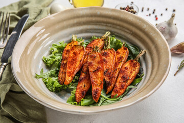 Bowl of tasty baked carrots with greens on table, closeup