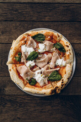 italian pizza with burnt sides on a wooden background top view. pizza with sausage, basil leaves, mozzarella and pistachios. sliced pizza close-up 