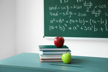 Apples with school books on table near chalkboard