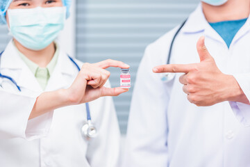 Two doctor woman and man holding vial corona vaccine bottle and pointing finger, coronavirus COVID-19 vaccination concept