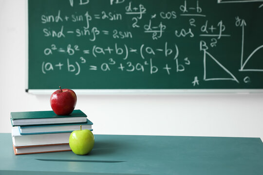 Apples with school books on table near chalkboard