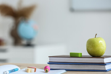 Apple with school books and erasers on table in classroom