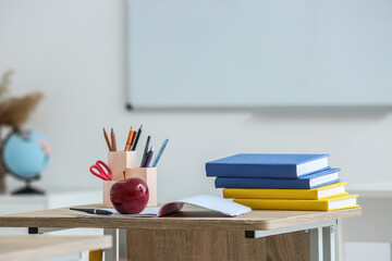 Apple with school books and pen cups on table in classroom
