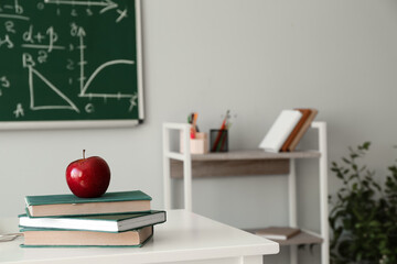 Red apple with school books on table in classroom
