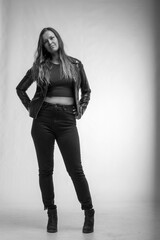 Woman in leather jacket and jeans standing on grey background in black and white