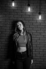 Young woman in leather jacket on a background of brick wall with vintage lamps in black and white