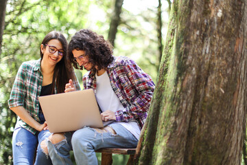 Young latin couple sitting in the forest looking and using laptop smiling at Costa Rica