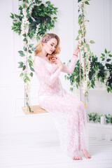 Young attractive bride with blond hair with wedding makeup and hairstyle in a white lace peignoir in a bright interior