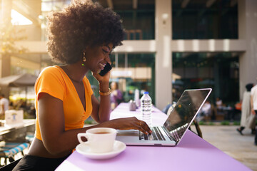 Happy beautiful young black woman using laptop in cafe