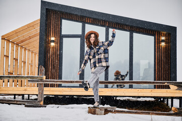 Curly young woman resting on terrace of modern barn house in the mountains. Happy female tourist...