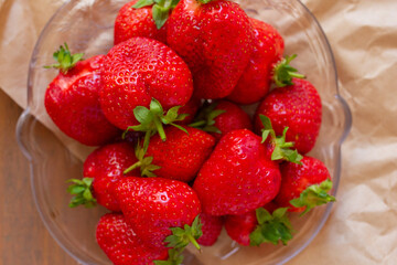Many red strawberries on glass plate and wooden table top view