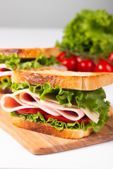 Close-up of two toasted sandwiches with fresh ham, cheese and vegetables on background. Club sandwich and take-away concept. Fast food. 