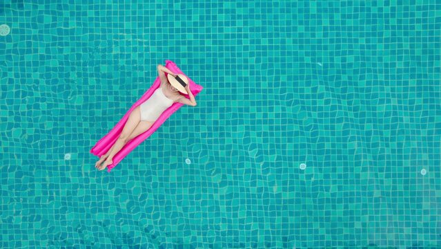 Top view of young asian woman in swimsuit on the pink air mattress in the swimming pool.