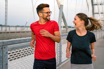 Early morning workout. Happy couple running across the bridge. Living healthy lifestyle.