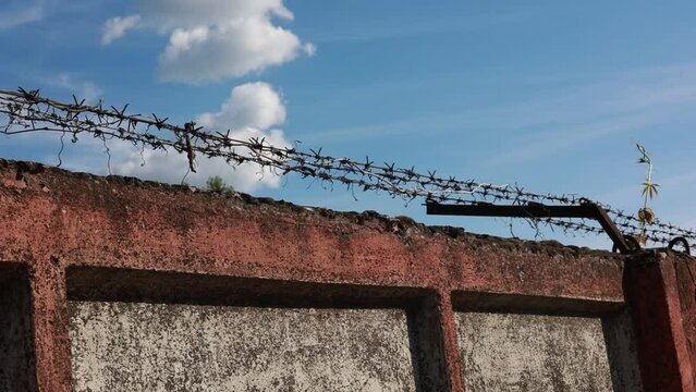 A concrete wall with barbed wire on a blue sky background
