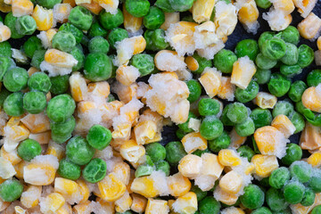 
Frozen green garden peas covered in ice on black surface with selective focus

