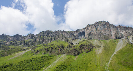 Mountain landscape with high stone cliffs and bright green grass on an alpine meadow in the Elbrus valley in the North Caucasus in Russia on a sunny summer day