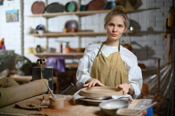 A ceramist makes a plate. Woman in an apron works in a pottery workshop. 