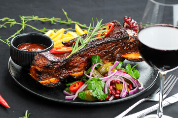 stewed ribs in a black plate with salad and potatoes with a glass of wine
