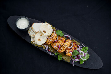 fried chicken shish kebab on a wooden board with flatbreads on a clean black background
