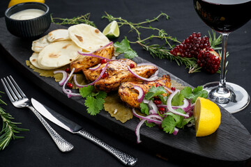 fried chicken shashlik on a wooden board with flatbreads on a black background with a glass of wine
