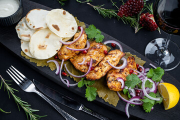 fried chicken shashlik on a wooden board with flatbreads on a black background with a glass of wine macro photo
