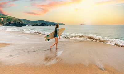Unrecognizable young surfer woman with wetsuit and surfboard entering the sea