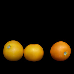 two yellow and one orange tomatoes on a black background