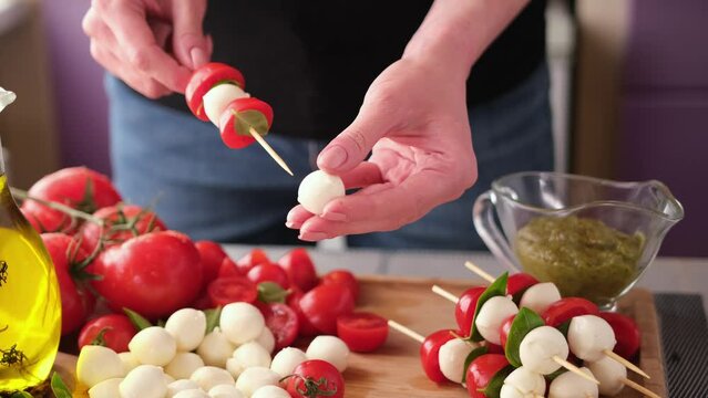 making caprese canapes sticking cherry tomatoes and mozzarella cheese balls on a skewer