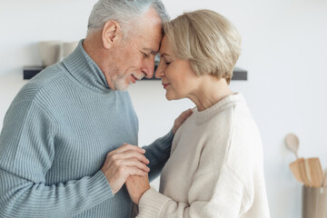 Elderly married couple hugging, standing together at home