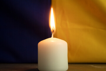 One burning candle against the background of the national flag of Ukraine