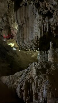 Inside the cave, which is poorly lit, a stream of water runs from large stalactites that have formed on the ceiling of the cave, which falls down, the video is vertical. High quality FullHD footage