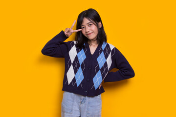 beautiful young asian girl showing peace or victory hand gesture on yellow background
